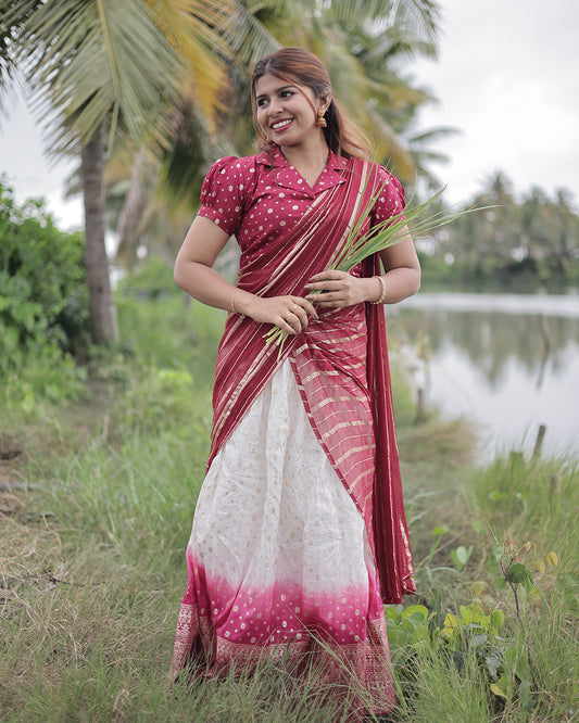 Woman in a red and white saree standing outdoors with greenery and water in the background